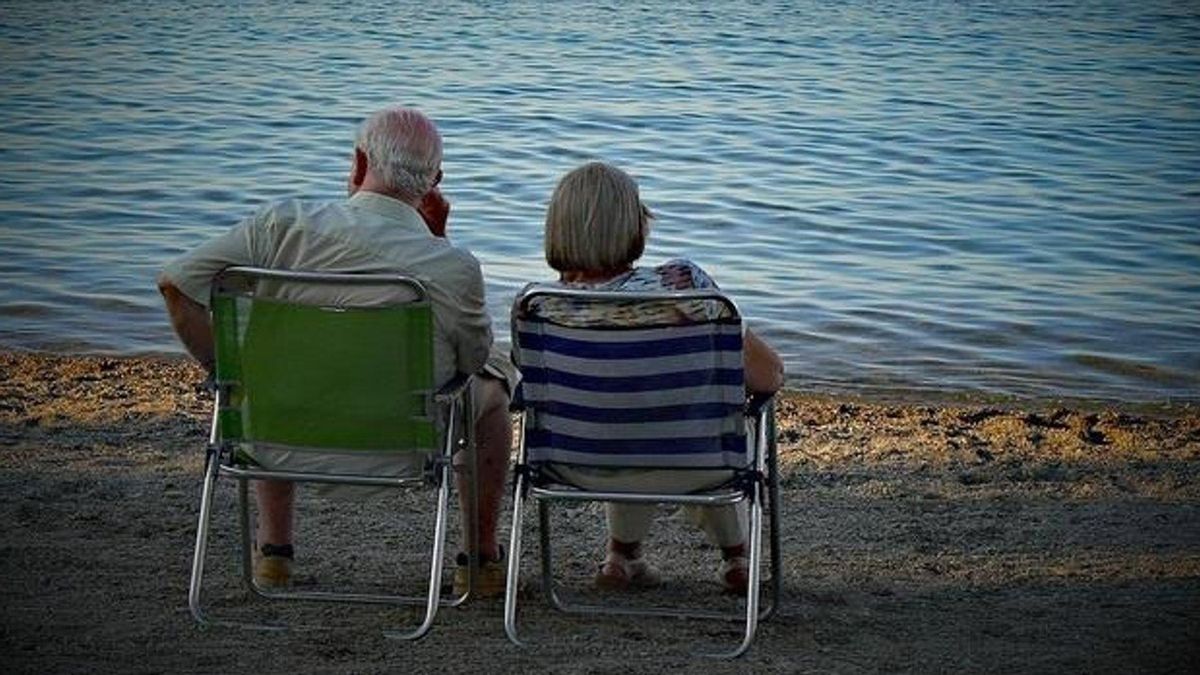 Dos personas mayores, sentados en una playa.