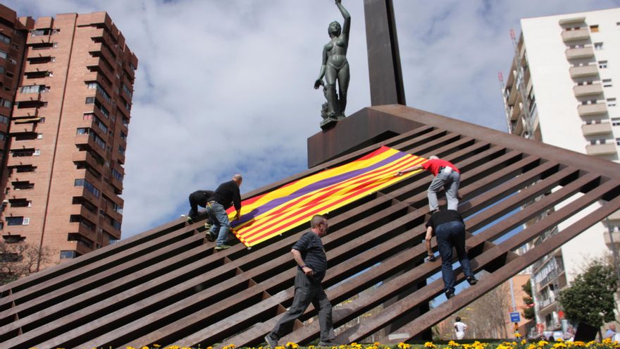 Varias personas colocan una bandera republicana junto a una 'senyera' en la plaza de la República, en Barcelona