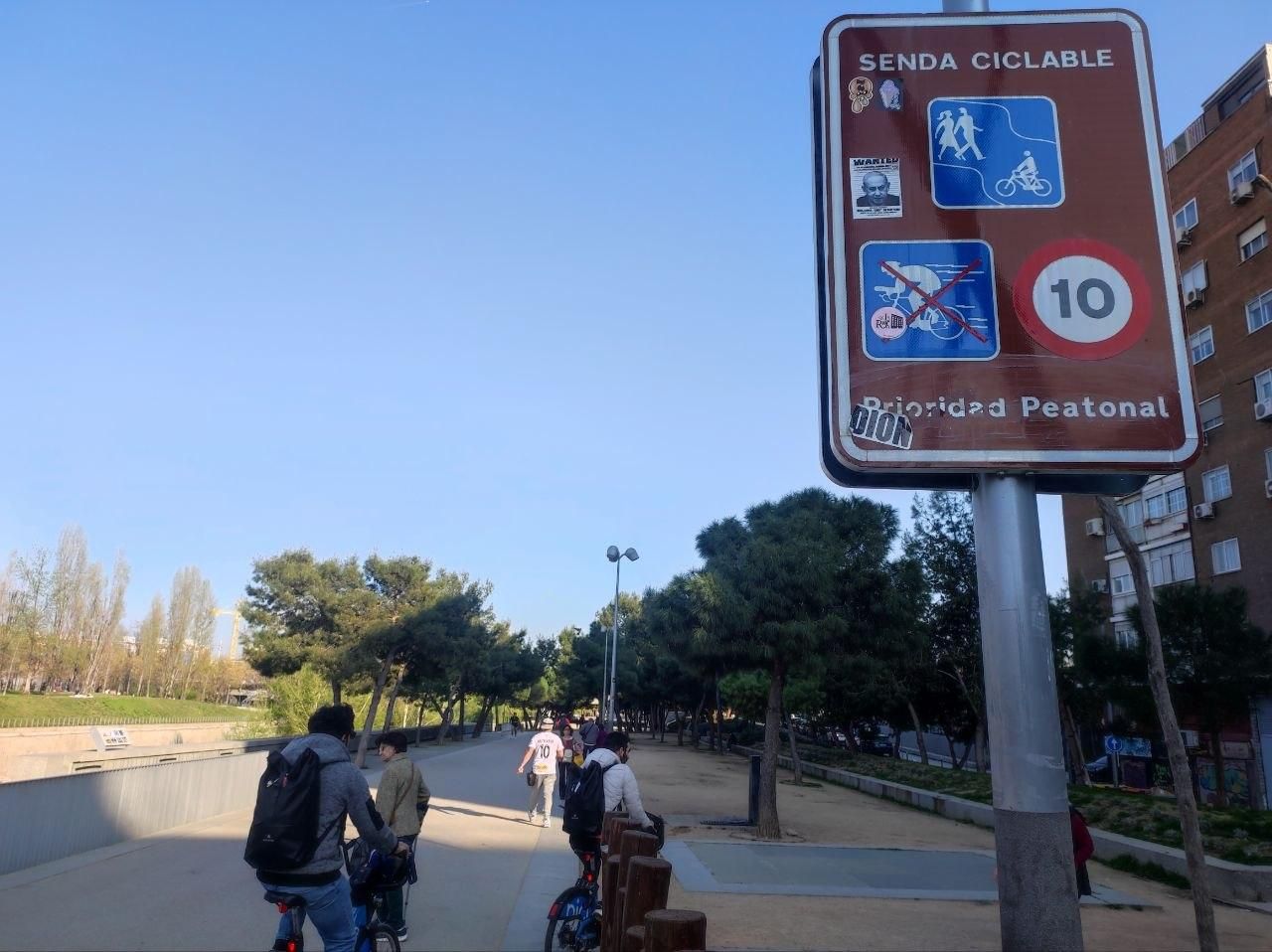 Cartel con las limitaciones a la actividad ciclista en Madrid Río junto a una zona de juegos infantiles y un acceso al parque.