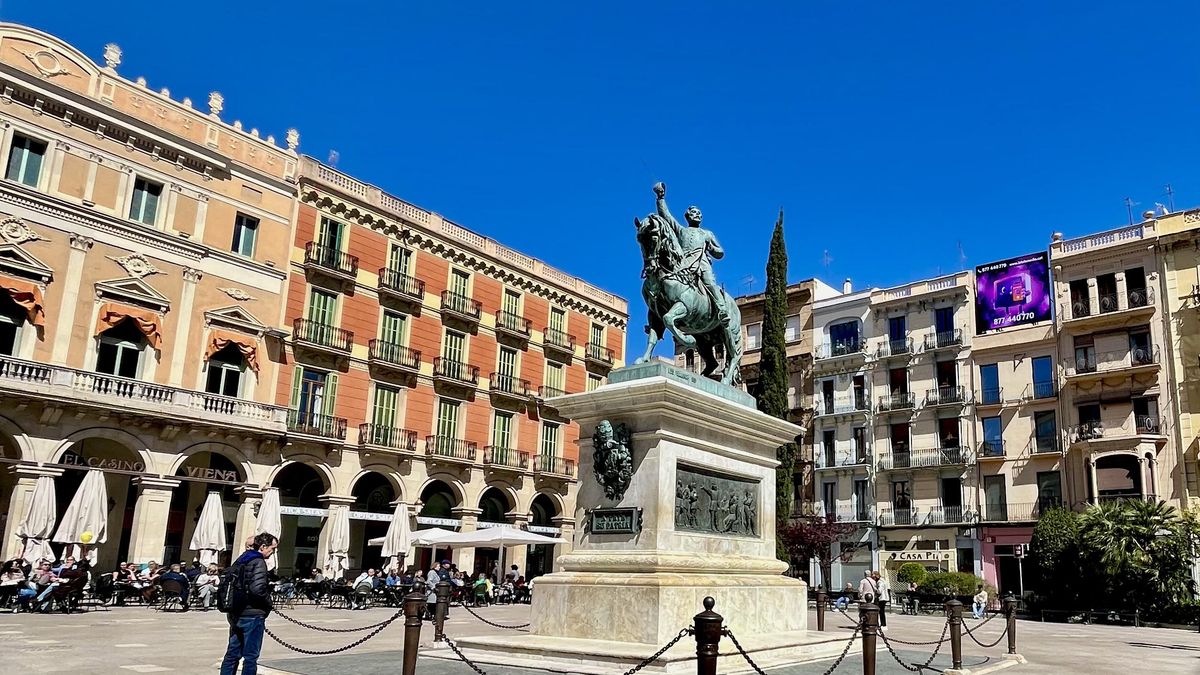Vista de la plaça Prim con la estatua como centro y el teatre Fortuny a la izquierda.