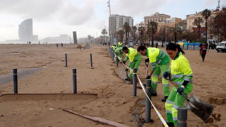 Trabajadores de la limpieza realizan su trabajo este jueves en la playa de la Barceloneta, gravemente afectada por la borrasca Gloria, que se ha cebado especialmente con el frente marítimo de Barcelona.