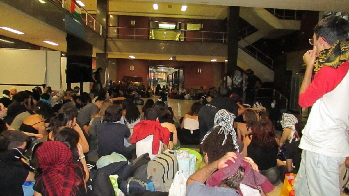 Los estudiantes escuchan el discurso del responsable del encierro sentados en el hall de la Facultad de Filosofía de la Universidad Complutense