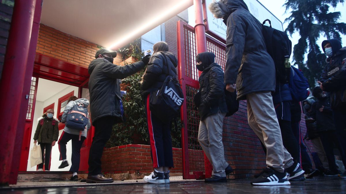 Un trabajador toma la temperatura a un alumno antes de entrar a un colegio.