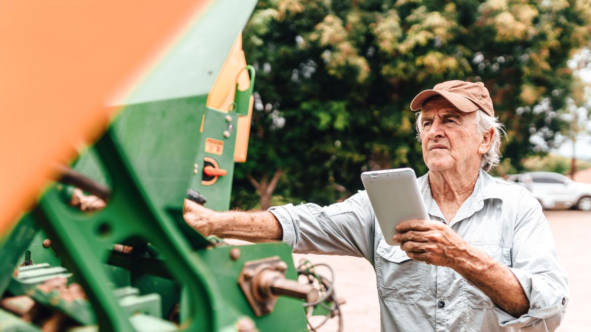 Agricultor que ajusta una máquina agrícola con una tableta