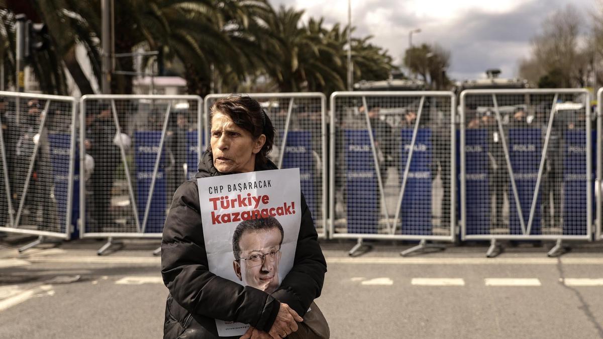 Una manifestante sostiene un cartel de Ekrem Imamoglu delante de una barrera policial.