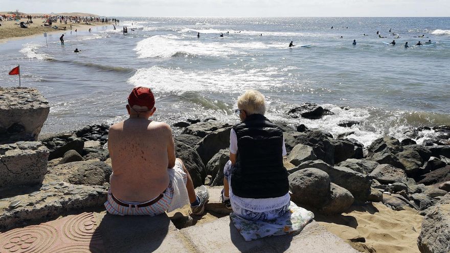 Una pareja de turistas observa a los bañistas este jueves santo en la playa de Maspalomas (Gran Canaria)