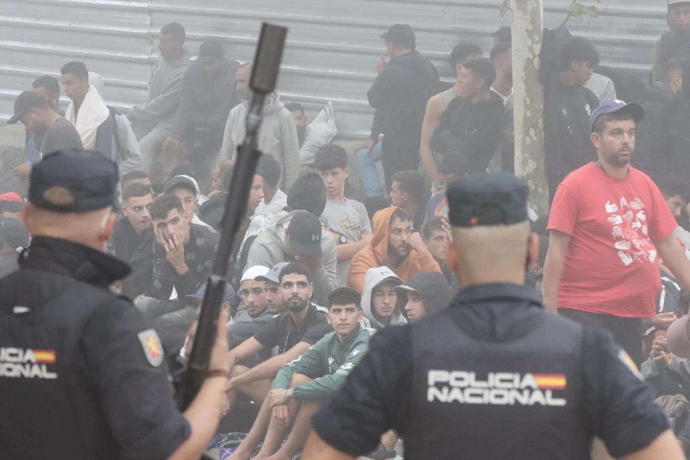 Policías vigilan a los migrantes que esperan en Loma Colmenar en Ceuta para poder acceder a un centro de acogida el miércoles.