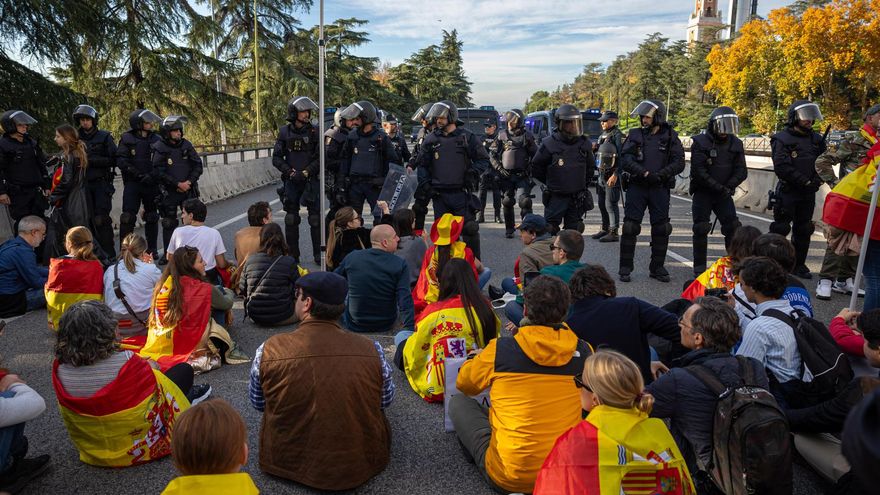 Unos jóvenes con banderas y pancartas protagonizan una sentada frente a efectivos de la Policía Nacional durante la manifestación que han trasladado hasta las inmediaciones de La Moncloa y los accesos de la A-6 a la capital, este sábado.
