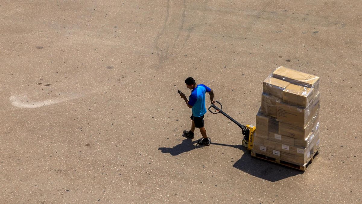 Un operario transporta varias cajas en València a pleno sol.
