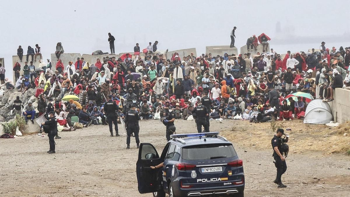La policía junto a centenares de personas que continúan viviendo en las inmediaciones de la playa del Trampolín en Ceuta, este viernes. EFE/Reduan