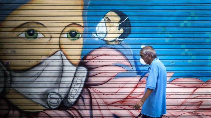 Un hombre con mascarilla pasa frente a un mural en Buenos Aires (Argentina).