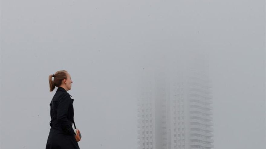 Una persona pasa junto a un edificio envuelto en niebla en Valencia.