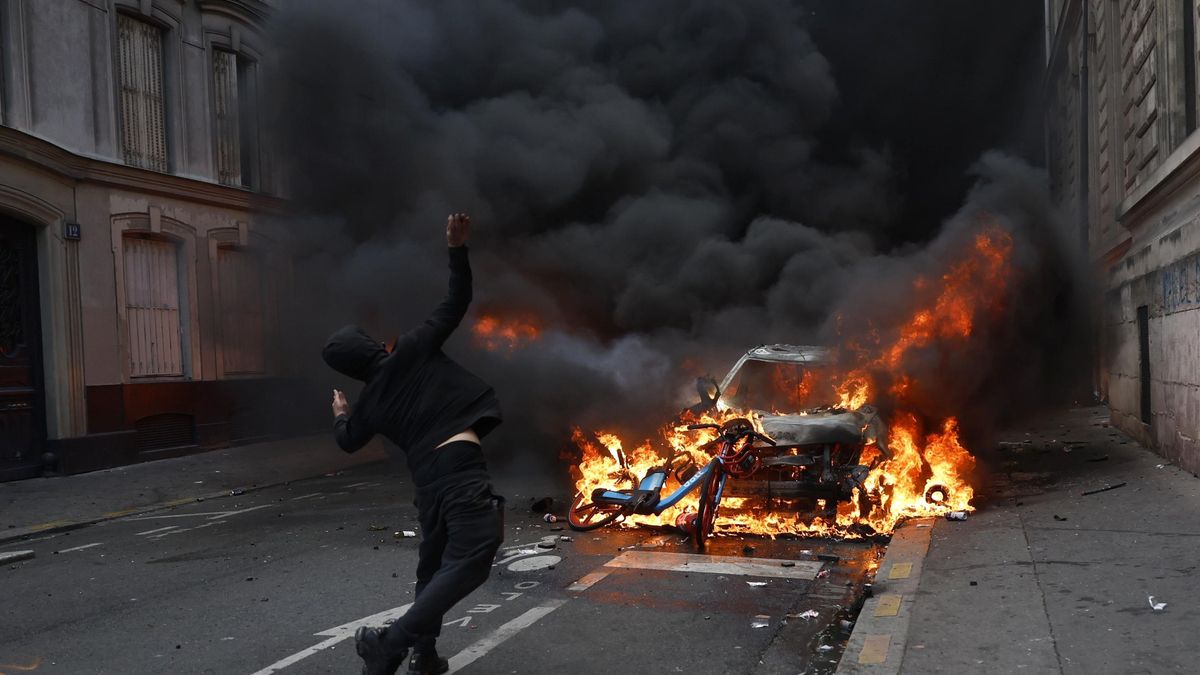 Un manifestante lanza proyectiles contra un coche en llamas durante una protesta contra el aumento del coste de la vida y los recortes en los servicios públicos en París.