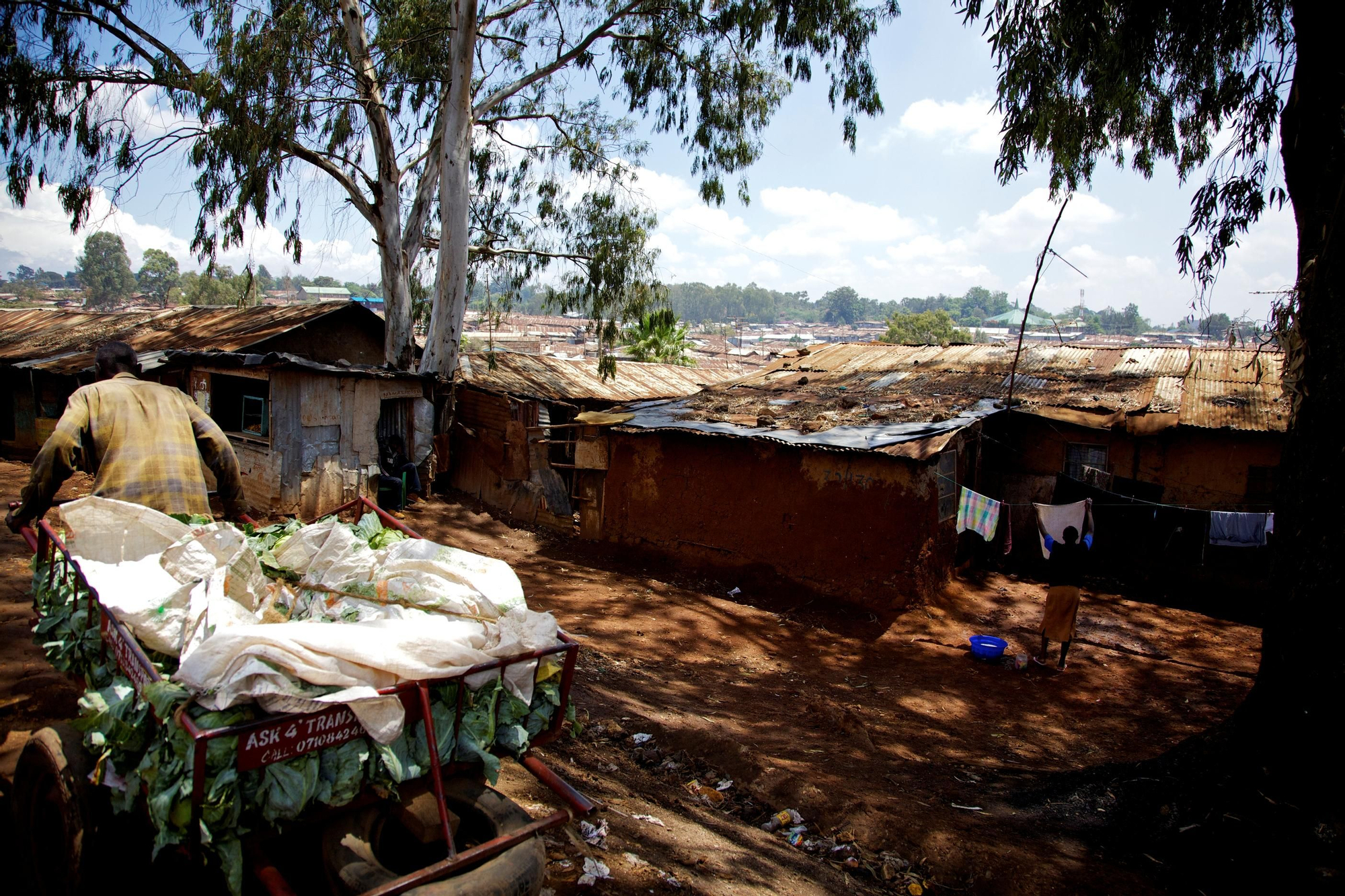 Un hombre acarrea su mercancía a través del suburbio. La elevada densidad, la deplorable higiene y la falta de agua limpia y drenaje incrementan significativamente el riesgo de propagación de enfermedades. Los residentes del suburbio tienen un acceso extremadamente limitado a servicios de salud.  Fotografía: Phil Moore
