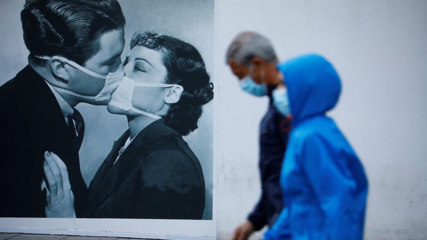 Unas personas protegidas con mascarilla pasan junto a un dibujo en la pared de un beso con mascarillas en una imagen de archivo. EFE/Salas