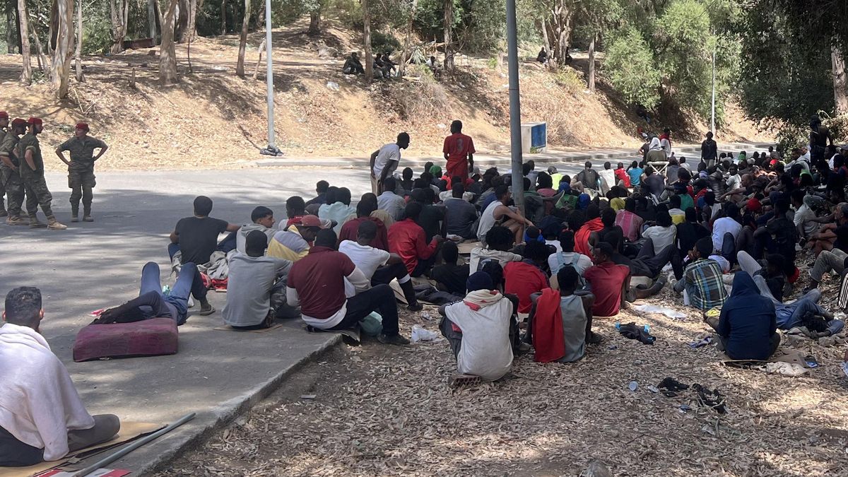 Un grupo de refugiados sudaneses se concentra en Ceuta ante la vigilancia de militares españoles.