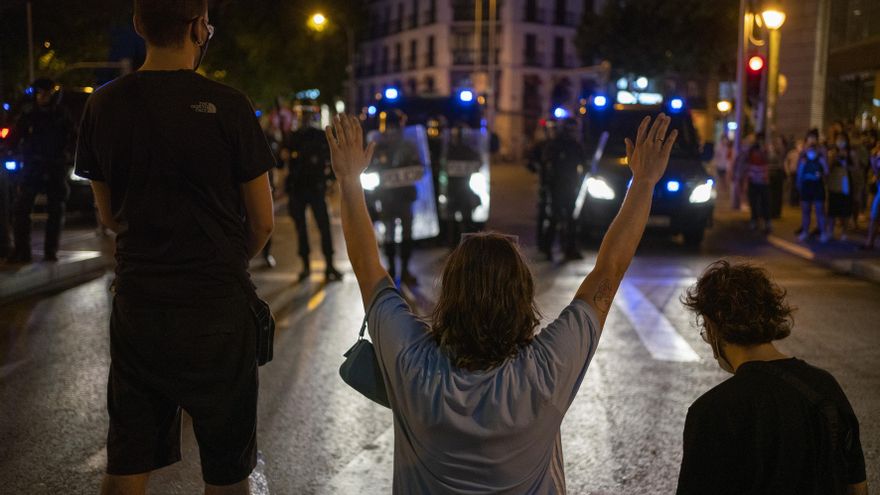 Un grupo de manifestantes protestan ante varios furgones policiales.