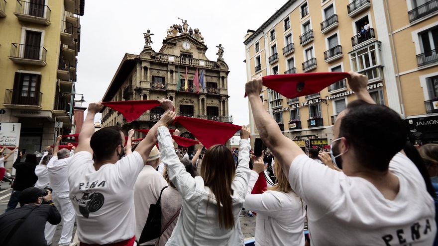 Varias personas levantan los pañuelos rojos a las 12 del mediodía en la plaza del Ayuntamiento de Pamplona, momento en que habría tenido lugar el tradicional chupinazo de San Fermín, suspendidos por segundo año por la pandemia