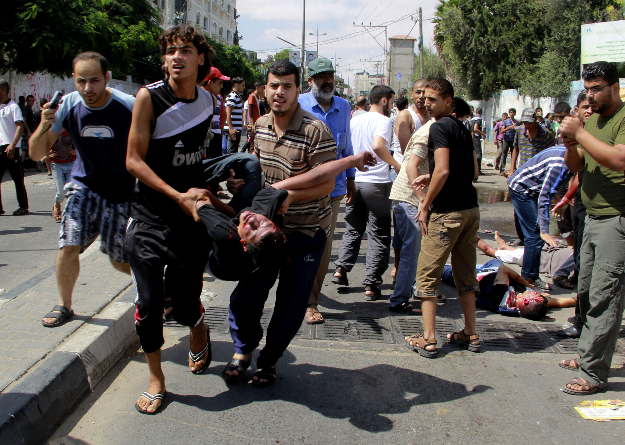 Dos palestinos portan el cuerpo de otro fallecido, en las calles aledañas a la escuela de la ONU para refugiados que ha sido bombardeada por el ejército israelí este domingo / Hatem Ali \ AP Photo