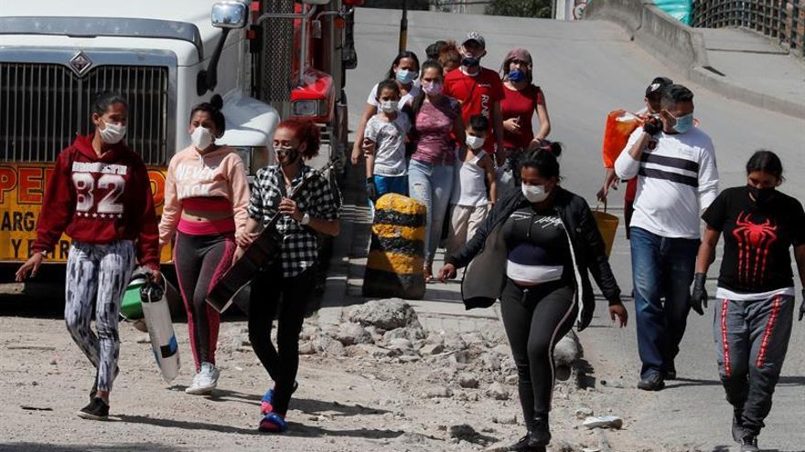 Un grupo de ciudadanos venezolanos camina cerca de los buses que fueron rentados por ellos mismos para regresar a su país ante la emergencia por el coronavirus COVID-19, pero que fueron devueltos por las autoridades colombianas el pasado domingo en Bogotá.