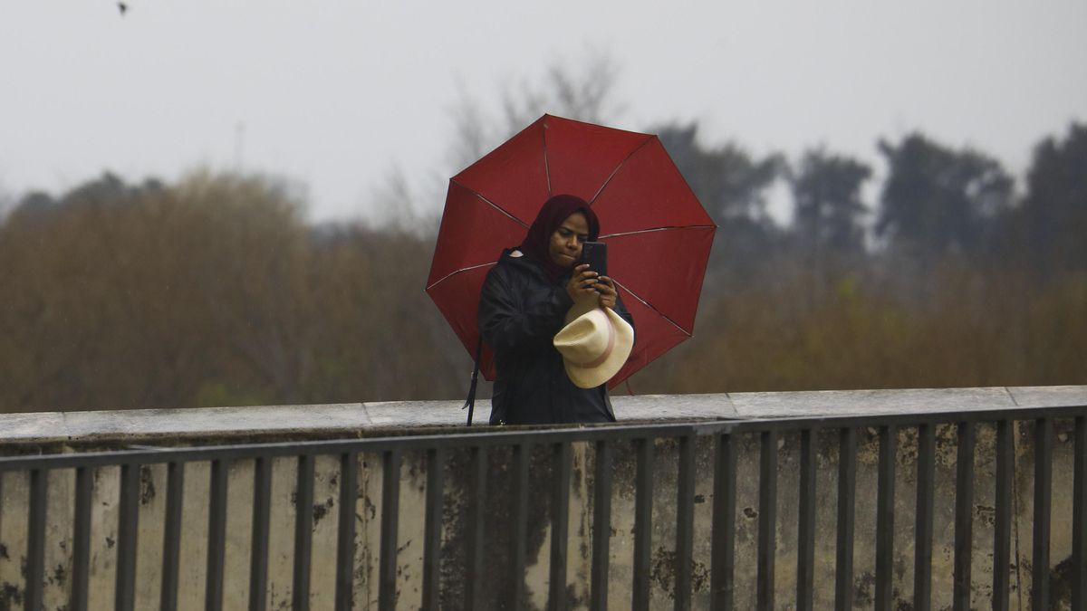 Una mujer se protege de la lluvia con paraguas mientras se fotografía en el puente Romano de Córdoba. EFE/Salas