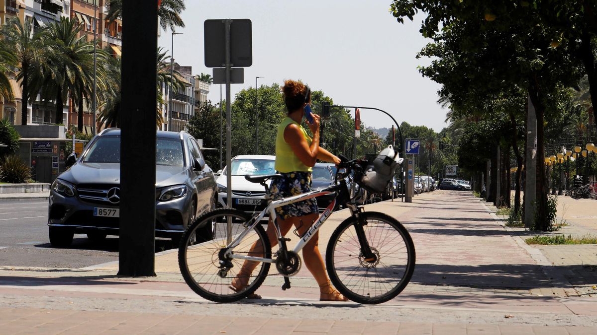 Persona camina por la calle en bici en día de temperaturas altas.