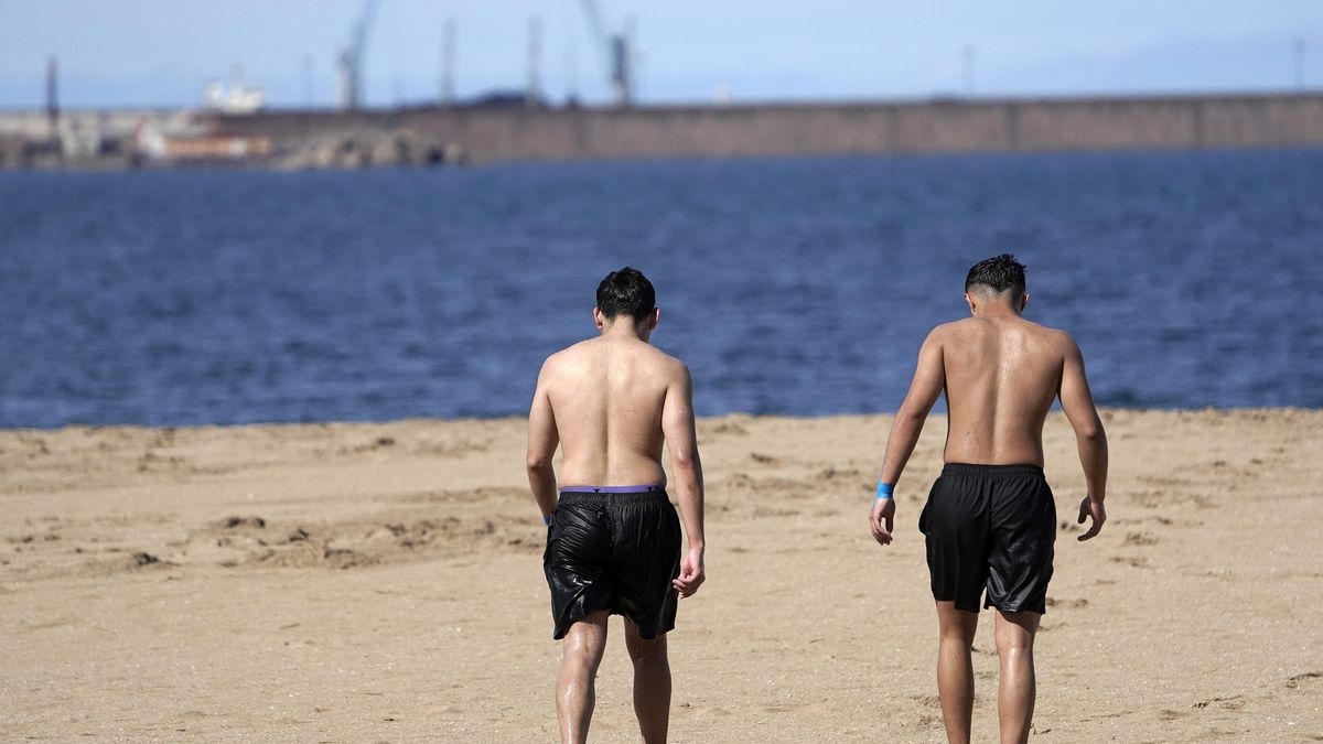 Dos jóvenes pasean por la playa de Poniente, en Gijón.