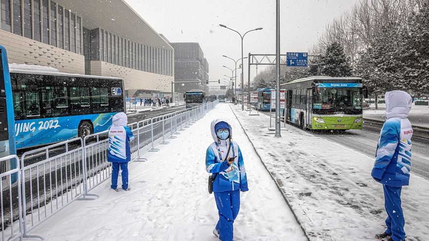 Voluntarios olímpicos se paran en una estación de autobuses frente al centro de medios olímpico en un día nevado, durante los Juegos Olímpicos de Pekín 2022 en Pekín, China.