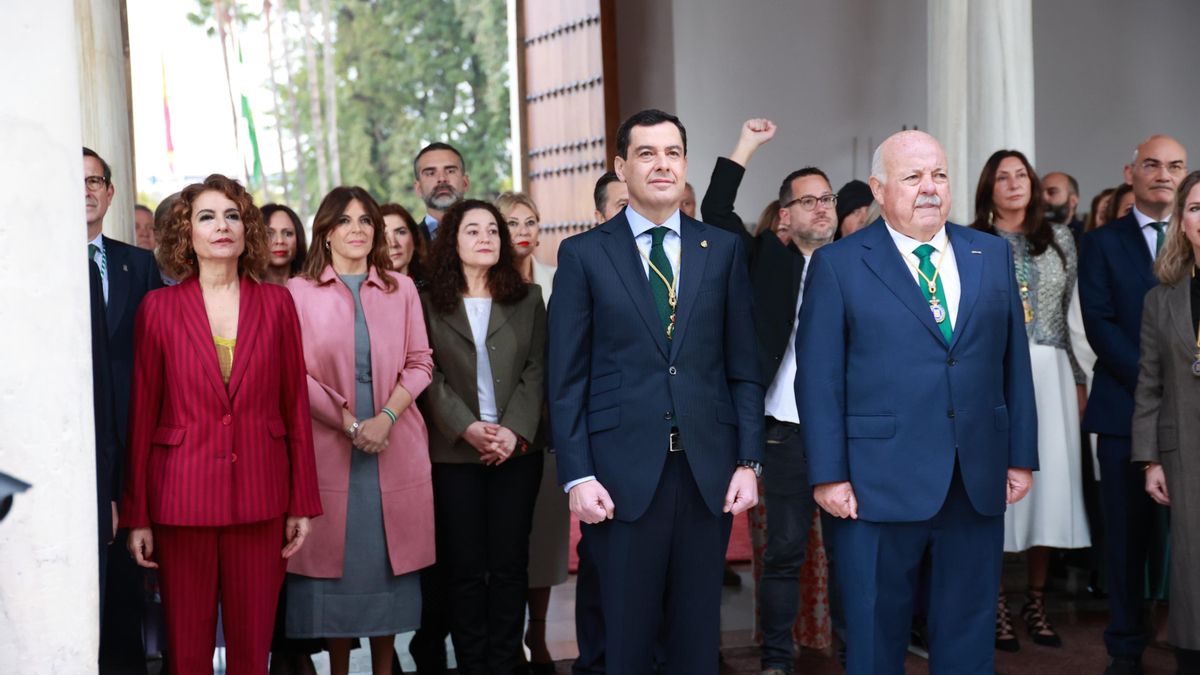 El presidente de la Junta, Juanma Moreno; el presidente del Parlamento, Jesús Aguirre; y la vicepresidenta y ministra de Hacienda, María Jesús Montero, siguen bajo la lluvia la interpretación del himno de Andalucía en el Parlamento por el 28F