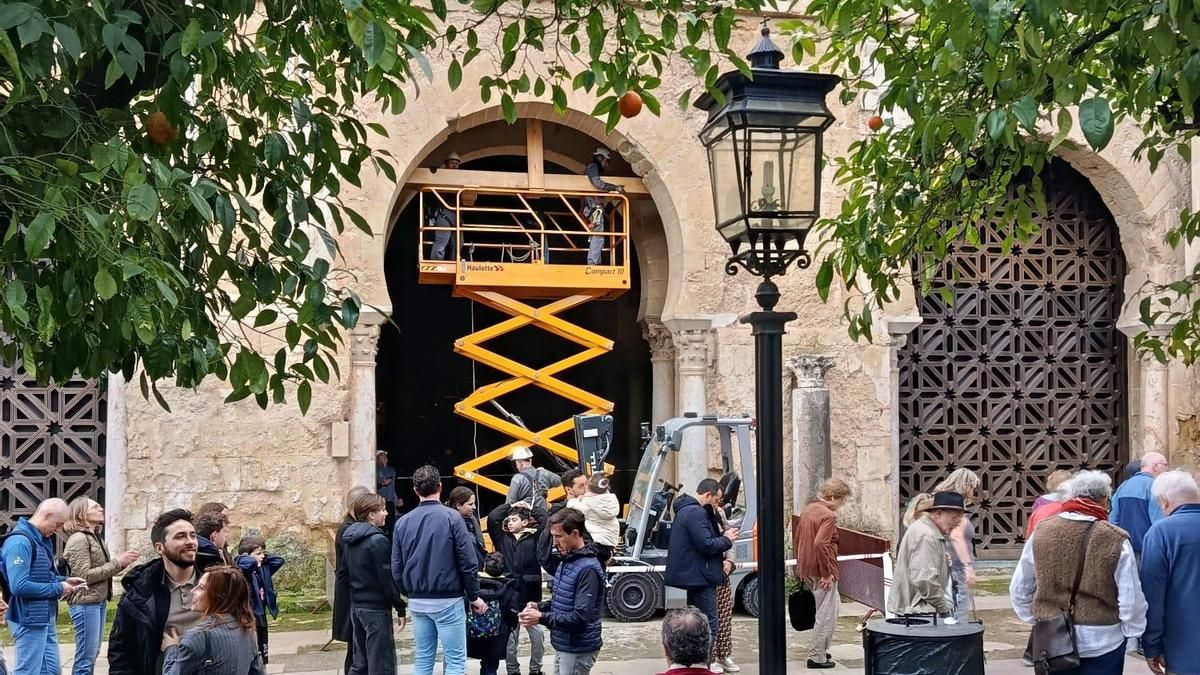 Operarios reponen la lona que tapa el hueco de la celosía retirada en el Patio de los Naranjos de la Mezquita.