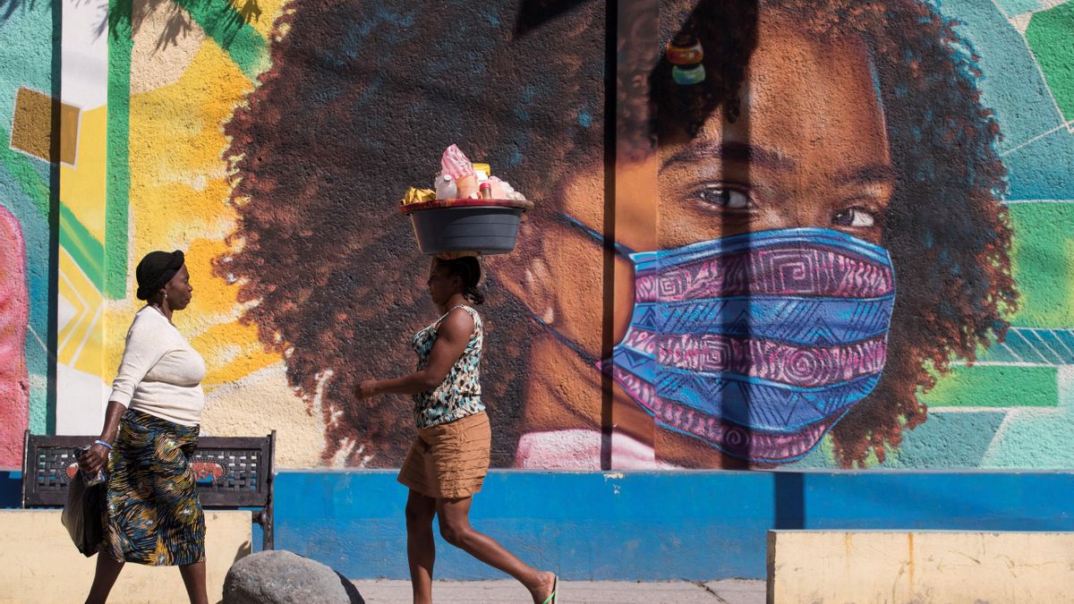 Dos mujeres caminan frente a un mural alusivo al uso del tapabocas por el coronavirus en Puerto Príncipe (Haití). EFE/ Orlando Barría/Archivo