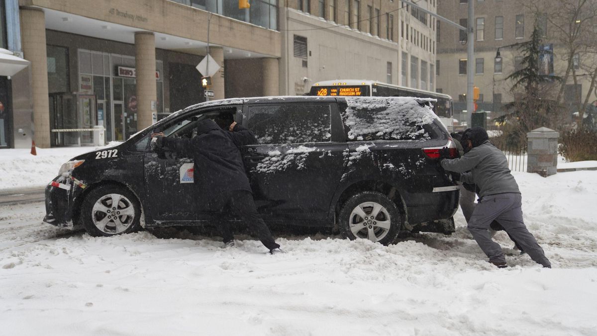 Personas empujando un automóvil atascado en la nieve, en Nueva York.