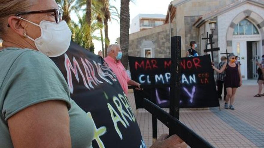 Una manifestante porta una cruz y una pancarta en la concentración de Los Urrutias