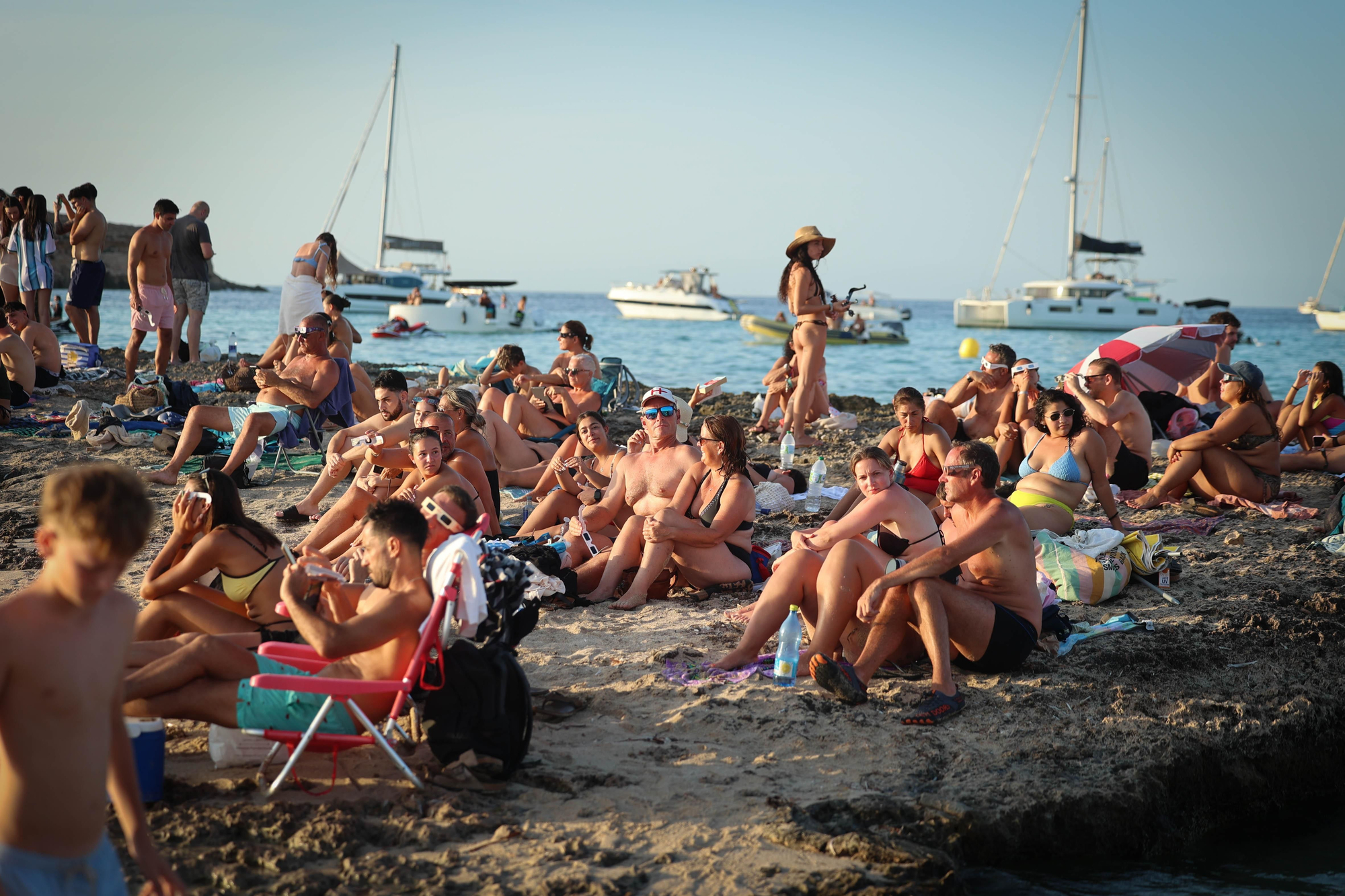 El ambiente festivo y expectante inunda la costa ibicenca con cientos de personas acomodadas frente a un mar repleto de barcos y yates