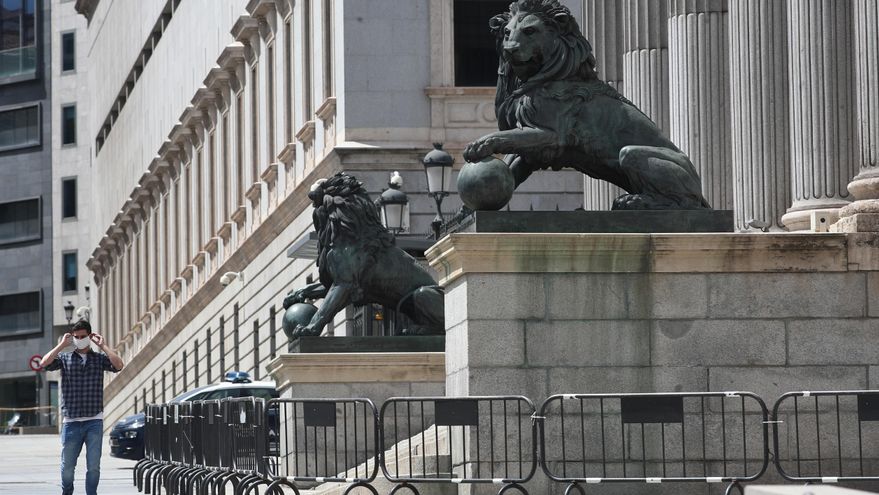 Un hombre se coloca una mascarilla mientras camina por delante de la fachada del Congreso