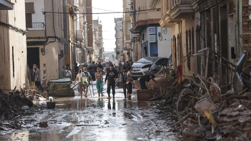 Varias personas caminan entre el lodo acumulado en las calles a causa de las intensas lluvias caídas por la fuerte dana, este jueves en Catarroja (Valencia).