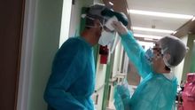 Una enfermera limpia la pantalla protectora a su compañero del Clínico.