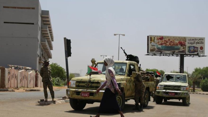 Una mujer camina junto a un vehículo de las Fuerzas de Apoyo Rápido en una intersección que lleva al cuartel general de las Fuerzas Armadas en Jartum (Sudán).