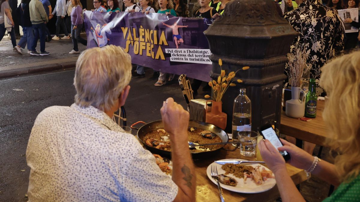 Una pareja de turistas cena en una de las calles del centro de València mientras transcurre la manifestación.