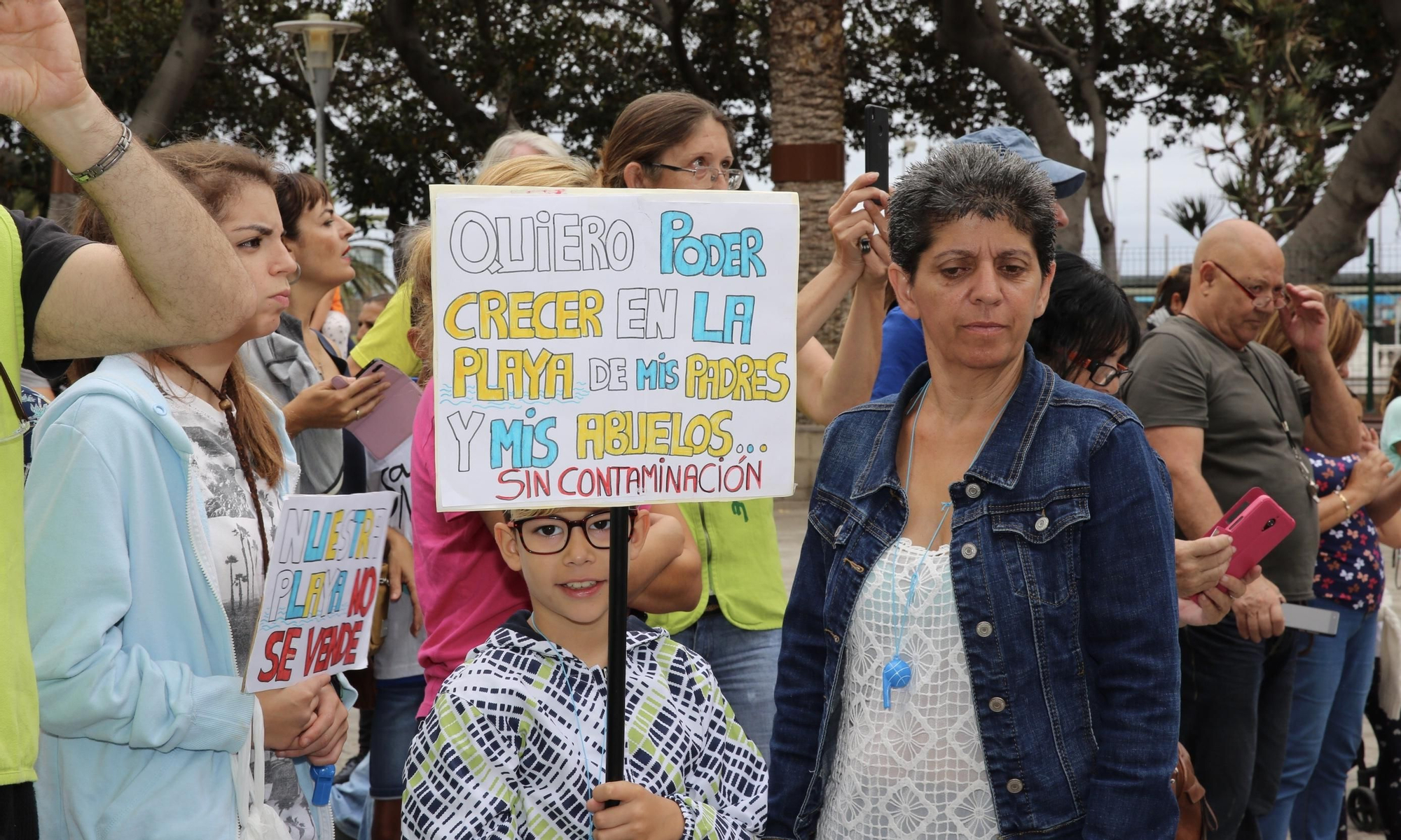 Un niño sostiene en una pancarta que quiere crecer en la playa de sus padres y abuelos.
