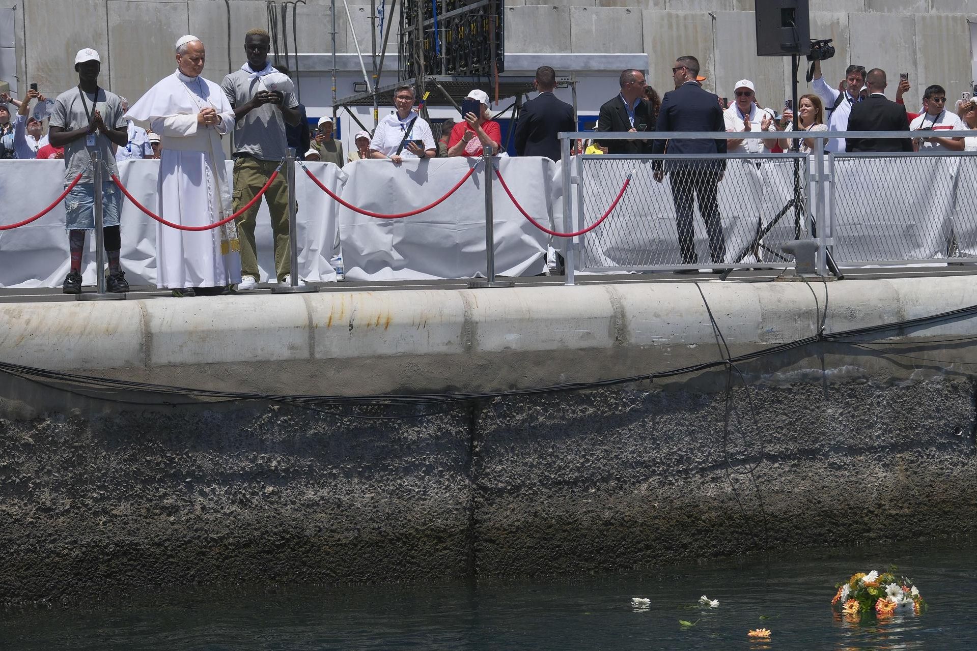 El Papa, junto a dos migrantes, realizando en el muelle de Arguineguín una ofrenda floral a los fallecidos en la Ruta Canaria.