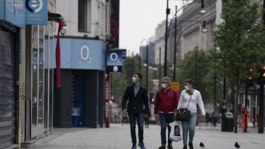 Varias personas caminan por una calle de tiendas de Londres, entre ellas una de telefonía de O2.