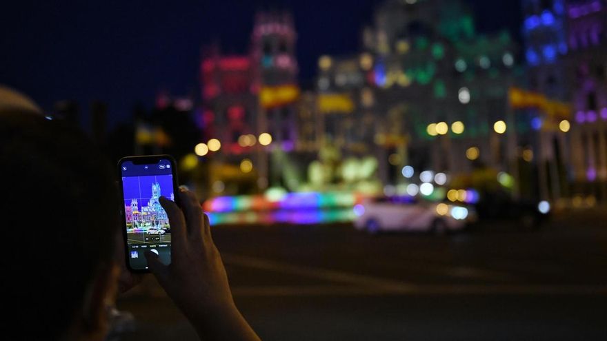 Una persona fotografía la fuente y el Palacio de Cibeles con los colores de la bandera LGTB, a 6 de julio de 2022, en Madrid