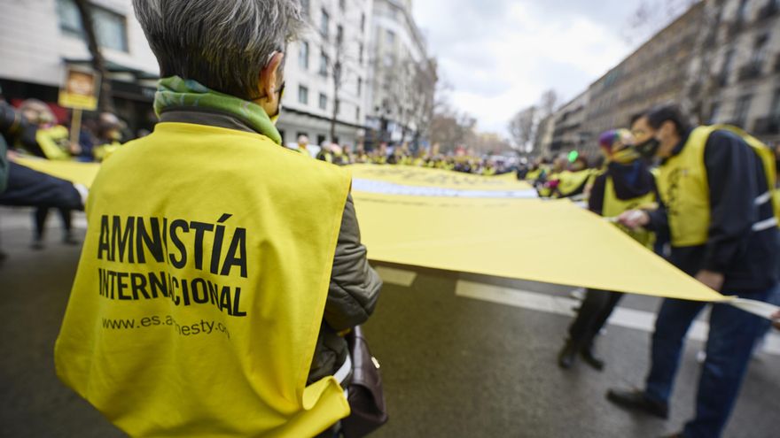 Varias personas portan una banderola amarilla gigante de Amnistía Internacional que reza 'Que ni los besos te callen' en una manifestación contra la ley mordaza.