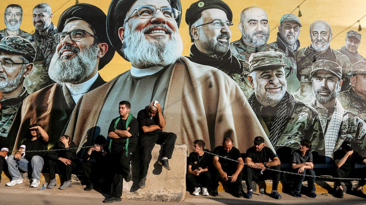 Partidarios proiraníes de Hizbulá se sientan frente a un cartel de los líderes del partido asesinados por Israel en un barrio del sur de Beirut. 