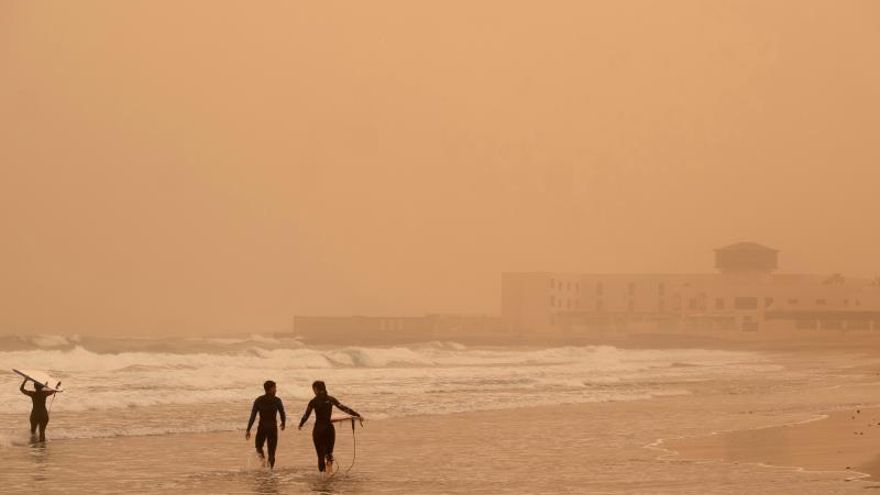 Varios surfistas se adentran en el mar de Playa Blanca, cubierta por una densa calima procedente de África, este domingo en Puerto del Rosario (Fuerteventura)..
