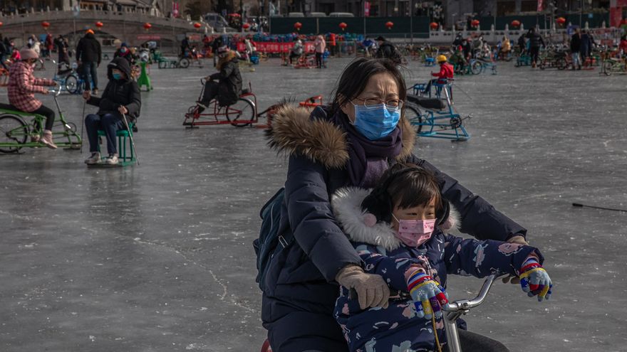 Una mujer con una mascarilla monta sobre una bicicleta de hielo con un niño en la espalda en la superficie congelada del lago Qianhai, en medio de la pandemia del coronavirus en Pekín, China. EFE/EPA/ROMAN PILIPEY
