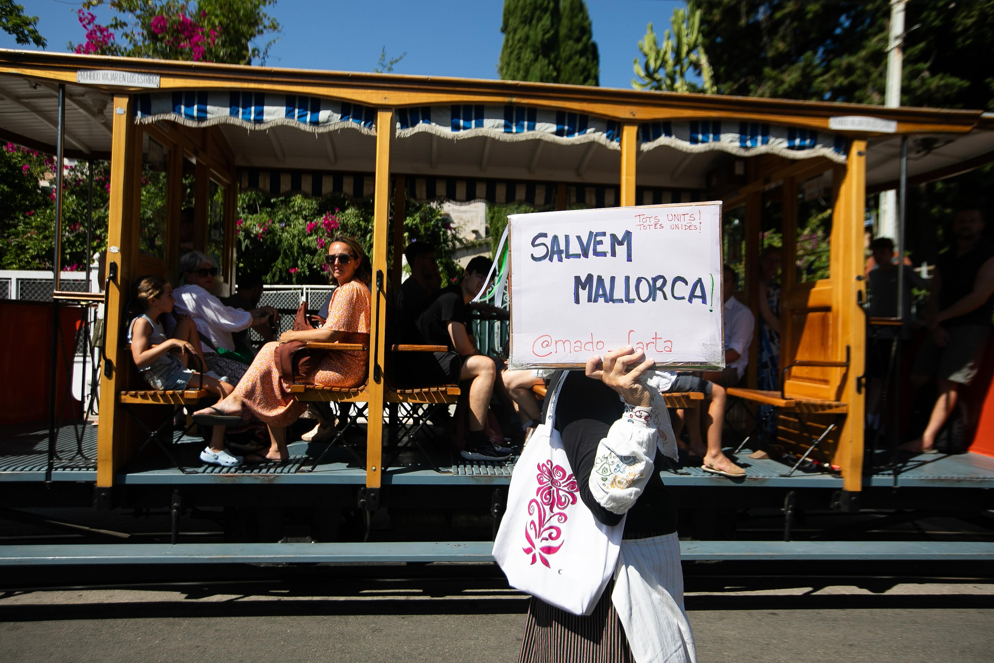 Turistas observan la protesta mientras uno de los manifestantes -popularmente conocido como 'Madó Farta'- exhibe una pancarta con el lema 'Salvemos Mallorca'