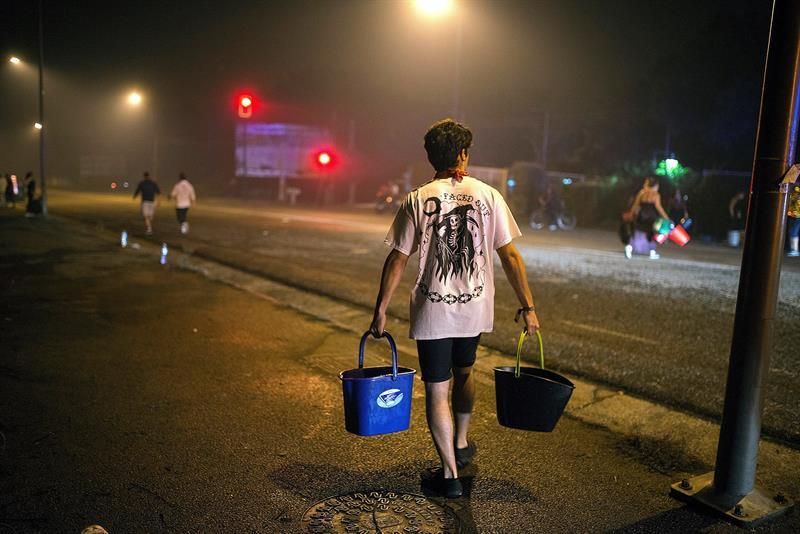 Un hombre porta dos cubos de agua para ayudar a sofocar uno de los focos declarados en el centro de la ciudad de Vigo. EFE