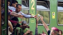 Un policía entrega zumo y frutas a los refugiados en la estación ferroviaria de Bicske (Hungría). / Efe.